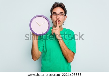 Young hispanic man holding a clock isolated on white background keeping a secret or asking for silence.