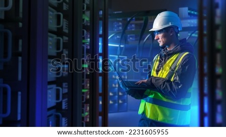 Man with laptop in server room. System administrator for industrial companies. Guy with computer. Server racks emit neon light. Maintenance industrial server equipment. Man in helmet in data center Royalty-Free Stock Photo #2231605955