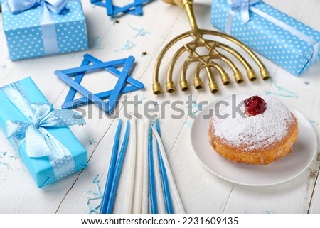Plate with tasty doughnut, candles and gifts for Hannukah celebration on white wooden background