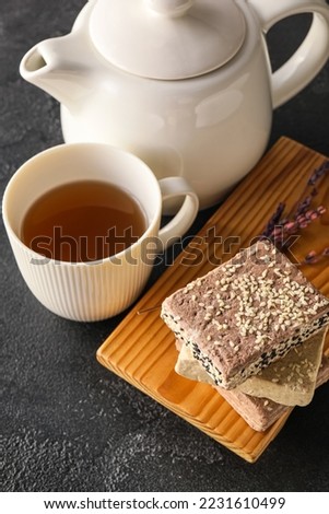 Wooden board with sesame halva, cup of tea and teapot on dark background, closeup