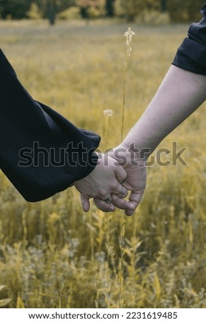 Close up spouses holds hands concept photo. Romantic gesture. Back view photography with rural meadow on background. High quality picture for wallpaper, travel blog, magazine, article