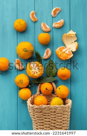 Orange juicy tangerine slices and peeled mandarines scattered on the wooden turquoise background. Flat lay. Copy space. Fresh summer vitamin rich fruits in a wicker basket