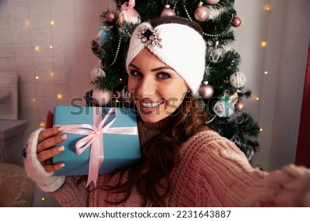 A happy young woman with a gift in her hand takes selfies against the Christmas tree. Merry Christmas and happy holidays New Year and Christmas concept.
