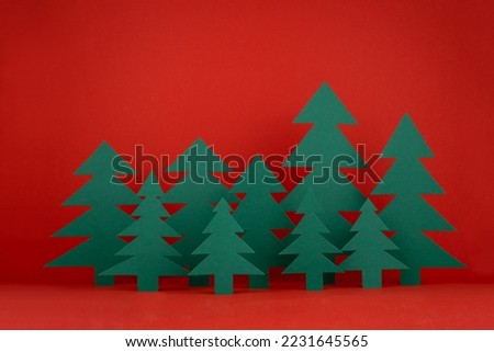 Bright Christmas background with paper green spruce forest on red backdrop in minimalist modern style. New year scene for presentation products and advertising text, card, poster, flyer.