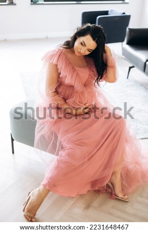 Beautiful pregnant woman in elegant dress posing to photographer in studio