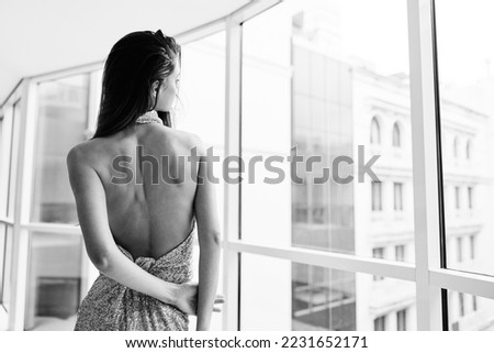 Woman in gold sequined dress by the window poses in a stylish image designer dress with open back, party look black and white photo