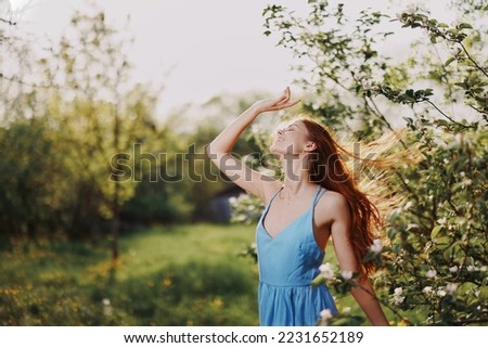 Woman with a beautiful smile with teeth and long hair flying hair spring dance hands up in the sunset in the park near the flowering trees happiness, natural beauty and hair health