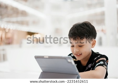 Little asian boy enjoying modern generation technologies playing indoors using tablet pc. Soft focus. Copy space.
