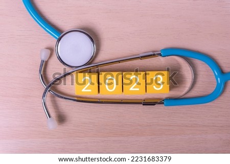 text 2023 year on wood cube building block and stethoscope , annual health check concept