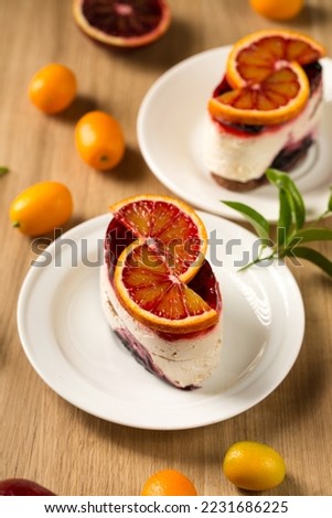 Panna cotta dessert with berry jelly and red orange on a white plate