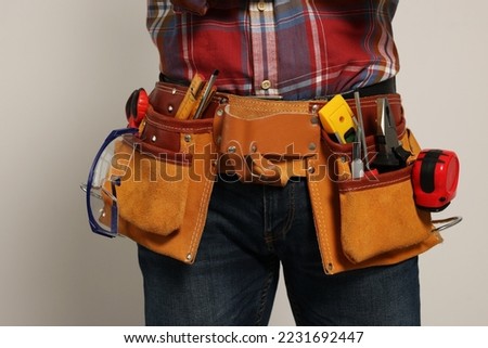 Professional builder with tool belt on light background, closeup Royalty-Free Stock Photo #2231692447
