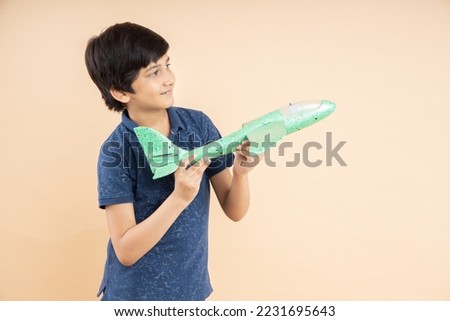 Happy playful indian boy kid holding airplane toy in hand isolated on beige studio background. copy space.