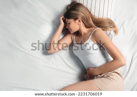Young woman suffering from menstrual pain in bed, top view. Space for text Royalty-Free Stock Photo #2231706019