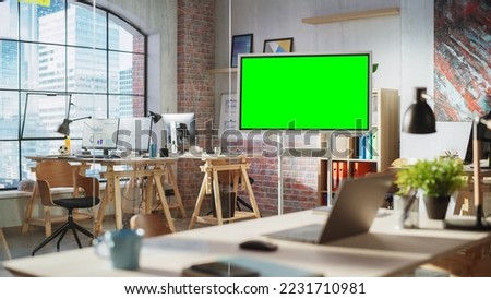 Empty Conference Room for Team Meetings in Modern Creative Agency with Art on Walls and Desks with Computers. Office Space with Digital Green Screen Mock Up Chroma Key Monitor for Presentations.