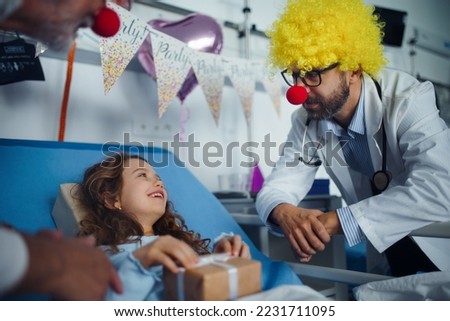 Happy doctor with clown red noses celebrating birthday with little girl in hospital room. Royalty-Free Stock Photo #2231711095