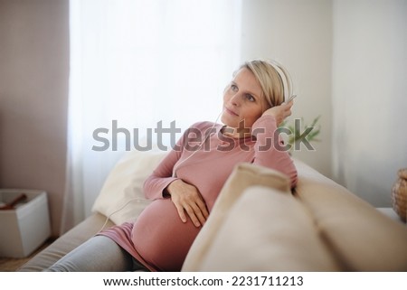 Pregnant woman sitting on sofa, listening music and enjoying time for herself.