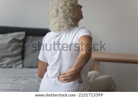 Rear view senior woman woke up touch lower back to reduce pain. Muscle spasm, tightness in pelvis, sharp ache kidneys infection, age related disease, osteoarthritis spinal stenosis treatment concept Royalty-Free Stock Photo #2231713399