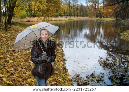 Blonde with a clear umbrella from the rain on an autumn day,Woman under a transparent umbrella on a cloudy autumn day on the lake shore,
