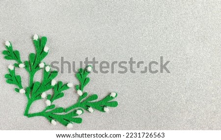 Green mistletoe branches on a silver glitter background, copy space. Christmas banner concept