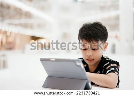 Little asian boy enjoying modern generation technologies playing indoors using tablet pc. Soft focus. Copy space.