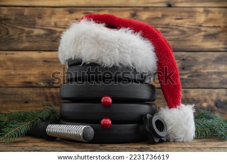 Dumbbell barbell weight plates in red Santa Claus Christmas hat, stacked on top of each other in shape of snowman. Healthy fitness holiday season winter composition. Gym workout sport training concept