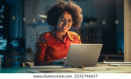 Young Black Female Working on Laptop Computer in Creative Office in the Evening. Multiethnic Project Manager Writing Emails, Getting Happy and Surprised When Receiving a Message from a Colleague. Royalty-Free Stock Photo #2231746657