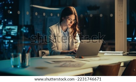 Stylish Female Working on Laptop Computer in a Company Office in the Evening. Young Manager Browsing Internet, Shopping Online and Reading Social Media Posts from Friends and Colleagues. Royalty-Free Stock Photo #2231746671