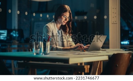 Office at Night: Focused Female Manager Working Long Hours Alone in Creative Agency, Implementing Business Strategy for Client. Creative Specialist Writing Corporate Project Plans on Laptop Computer.