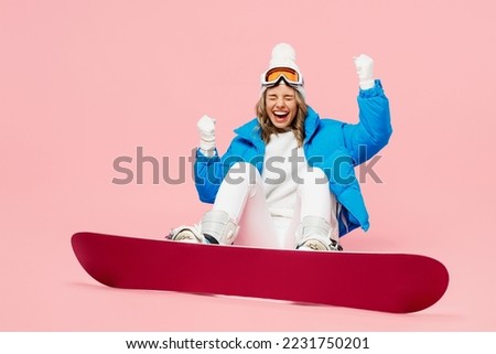 Bottom view snowboarder woman wear blue suit goggles mask hat ski padded jacket sit do winner gesture isolated on plain pastel pink background. Winter extreme sport hobby weekend trip relax concept