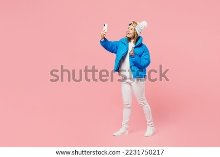 Sise view snowboarder woman wear blue suit goggles mask hat ski padded jacket do selfie shot mobile cell phone show v-sign isolated on plain pink background Winter extreme sport hobby relax concept