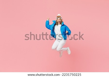 Snowboarder happy woman wear blue suit goggles mask hat ski padded jacket do winner gesture jump high isolated on plain pastel pink background. Winter extreme sport hobby weekend trip relax concept