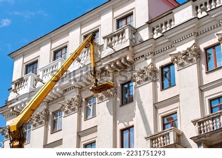 Construction worker in lift bucket crane restore and repair historic facade of building. Man in cradle, restoring plaster decoration, repair balcony. Workers painting building, renovating work Royalty-Free Stock Photo #2231751293