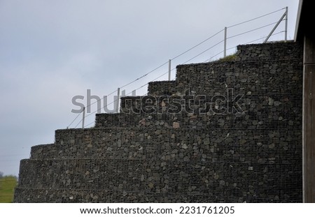 gabion retaining walls at the highway underpass highway embankment. the body of the highway is grassy from the guardrails to the toe with strips of bushes strengthening the soil against landslides Royalty-Free Stock Photo #2231761205