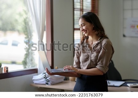 Beautiful Asian business woman standing holding a laptop in the office