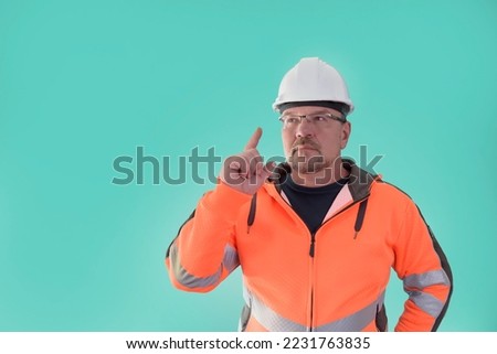 A male builder, thinking, finger up, in work clothes and a construction helmet, on a light green background. 