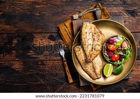 Roasted Gilthead Sea Bream fillets served with fresh vegetable salad. Wooden background. Top view. Copy space. Royalty-Free Stock Photo #2231781079