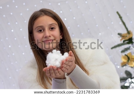 teenage girl holding artificial snow in her hands looking at the camera smiling in a winter white fur coat, photo with a shifted horizon line