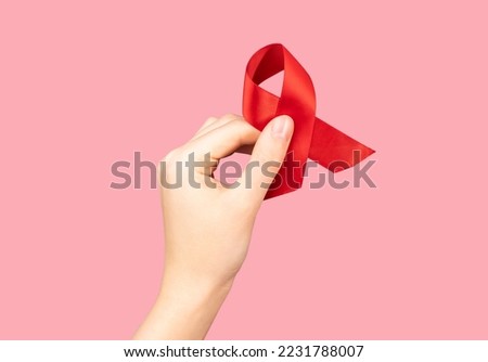 Red satin ribbon, bent loop in hand on pink background. HIV and AIDS awareness day, 1 December symbol. High quality photo
