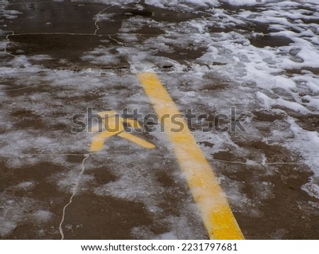 Yellow traffic sign under ice. Asphalt road for pedastrians marked with special sign. Pedestrian Symbol Painted over gray Asphalt with snow and ice. Permission to move people. Danger, slippery.