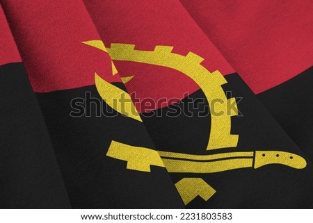 Angola flag with big folds waving close up under the studio light indoors. The official symbols and colors in fabric banner
