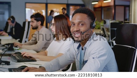 African American young man in headset talking with client at computer. Call center concept. Portrait of happy male support worker looking at camera and smiling. Job in sales. Selling by phone. Royalty-Free Stock Photo #2231810813
