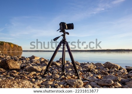 Professional camera on tripod at rocky lakeside Royalty-Free Stock Photo #2231813877