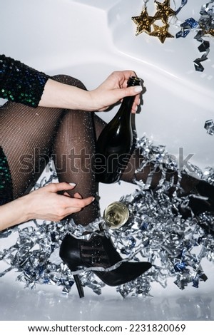 New Years Party celebration. Happy young woman in evening dress sitting in the bathtub drinking champagne and having fun