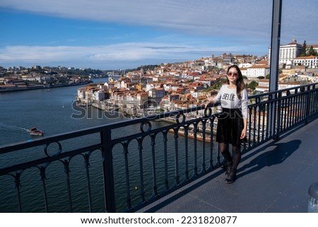 Young woman walking through the Dom Luís I Bridge with striped white shirt with the text in French "Belle Nouvelle" that means nice news