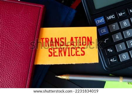 On a light background, gold-framed glasses, a flower in a pot, a green notebook, a red pen and a brown notebook with the text TRANSLATION SERVICES. Business concept Royalty-Free Stock Photo #2231834019