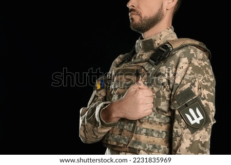 Soldier with Ukrainian trident on military uniform against black background, closeup. Space for text