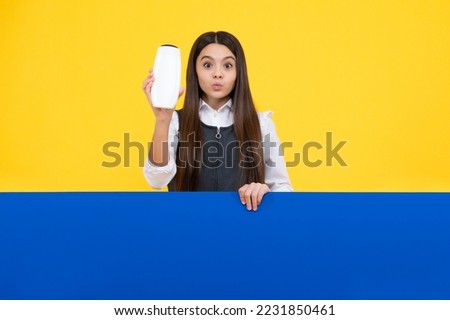Teen child girl with shampoo bottle or shower gel isolated on yellow background. Kids hair cosmetic product.