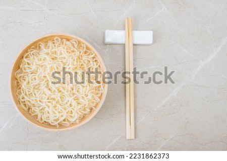 White bamboo plate (bowl) with egg noodles and chopsticks on a light background. Asian traditional fast food