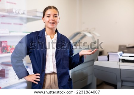 Happy young woman in blue robe uniform sticking out her left hand to show the workflow in the printer house