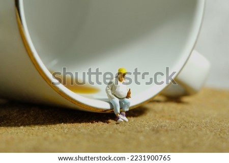 Miniature people toy figure photography. Fat men worker take a break rest sitting in front cup of coffee. Image photo